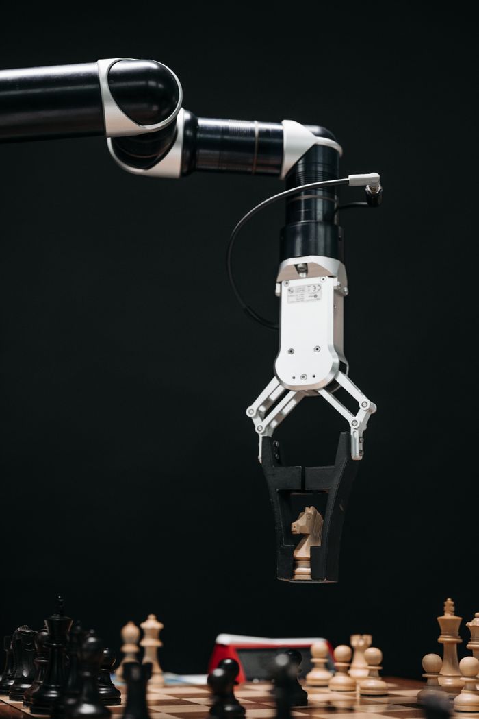 A robotic arm with a pincers holding a knight chess piece on a chessboard.